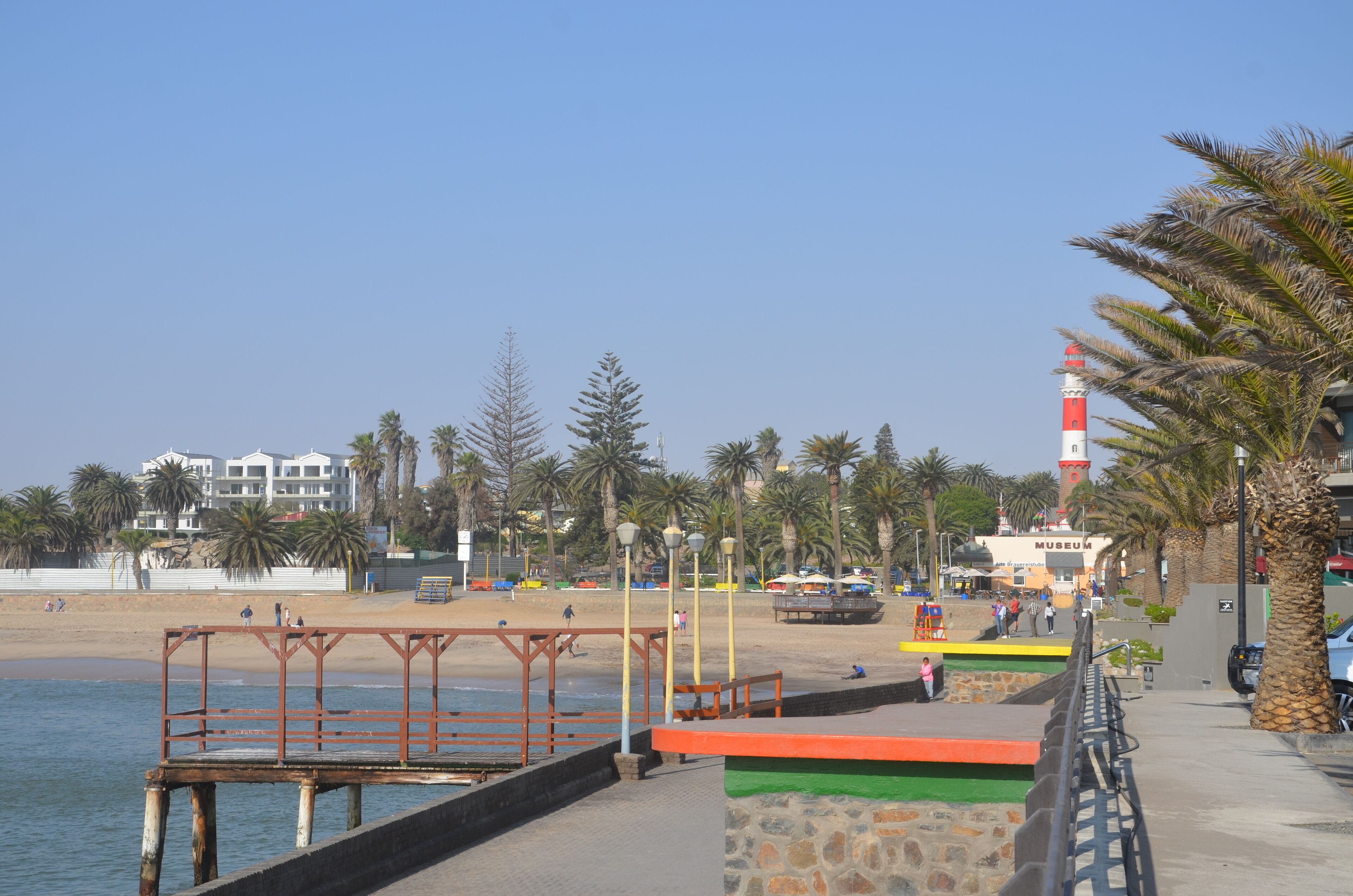 Un paseo marítimo con playa, palmeras y un faro.