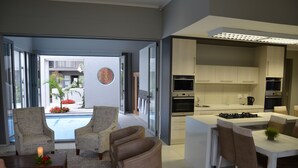 A modern kitchen with a central island, a dining area with chairs, and a living area with sofas and a coffee table. - Be Still Accommodation (Swakopmund)