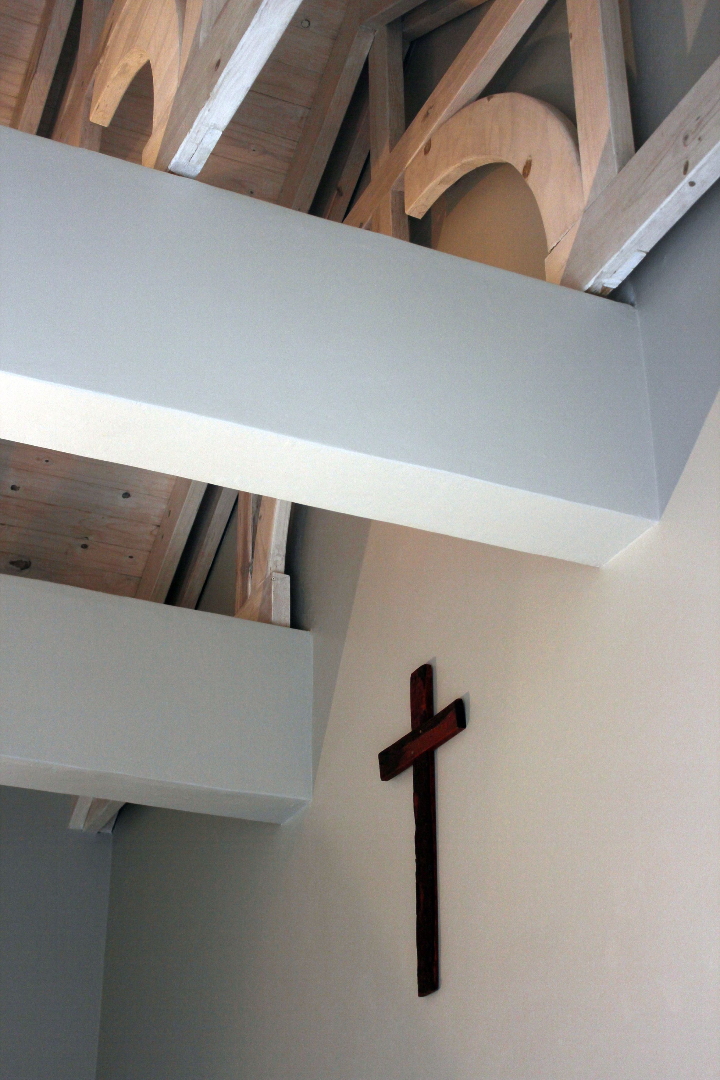 A wooden ceiling with exposed beams and a white wall with a wooden cross.