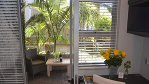 A room with a wicker chair, a small table with a bottle and glasses, a vase with yellow flowers, and a 'No Smoking' sign. - Be Still Accommodation (Swakopmund)