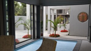 A modern indoor pool area with a glass wall, a pool with a blue mat, and potted plants. - Be Still Accommodation (Swakopmund)