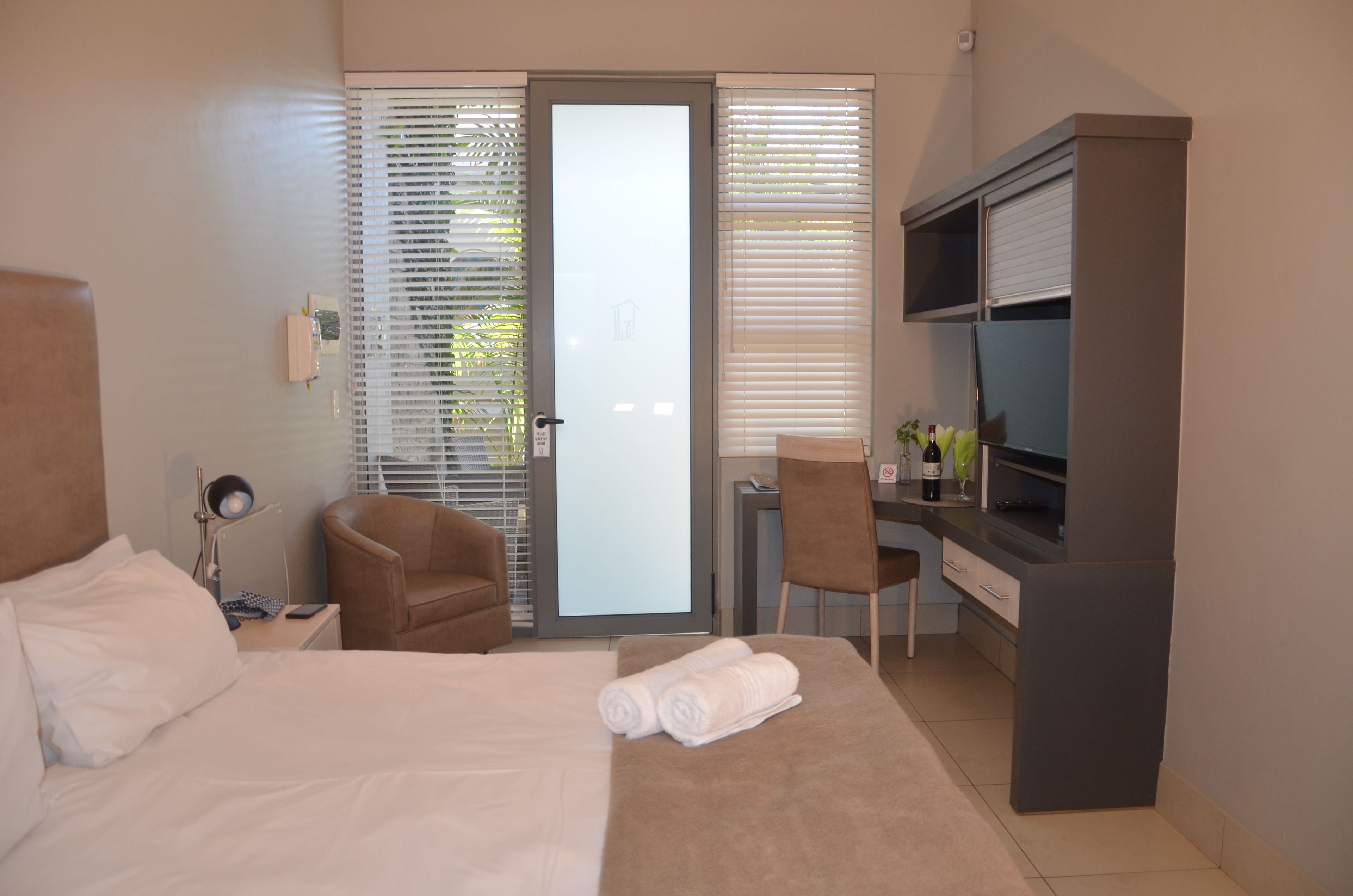Una camera d'albergo con un letto, una scrivania, una sedia, una televisione e una porta-finestra scorrevole verso l'esterno.