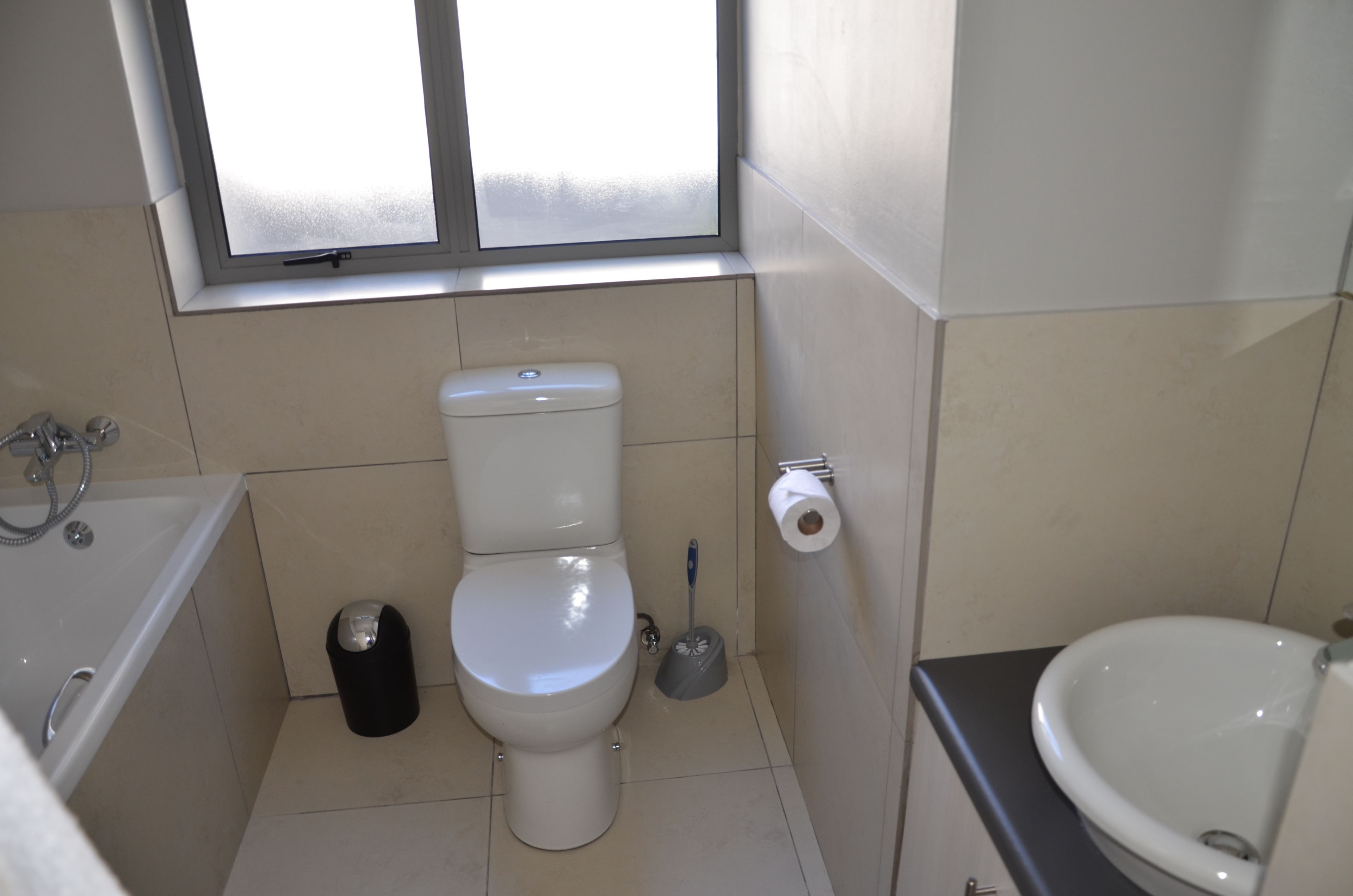 A small bathroom with a toilet, a bidet, a sink, and a window above the toilet.