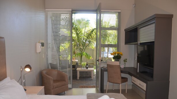 A hotel room with a bed, two chairs, a desk, a television, and a view of the outdoors. - Be Still Accommodation (Swakopmund)