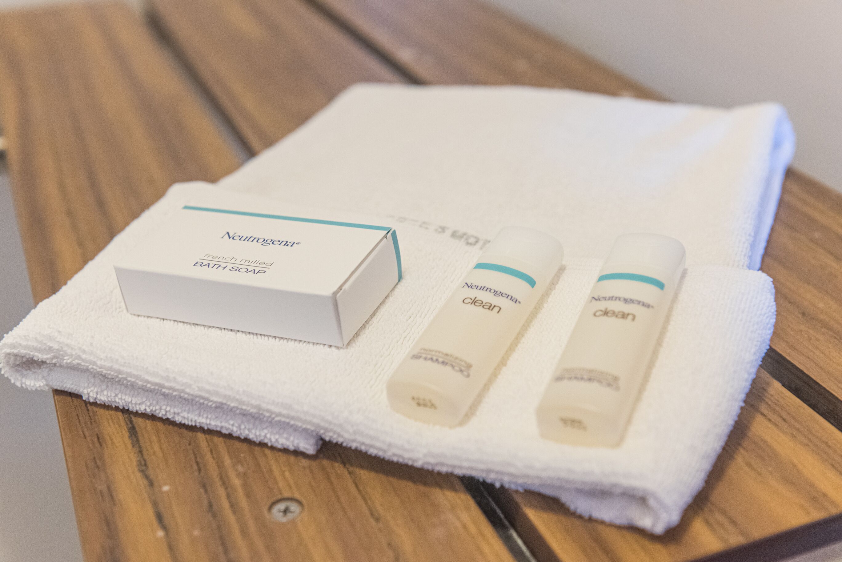 A white Neutrogena bath soap box and two tubes of Neutrogena clean body wash on a white towel on a wooden table.