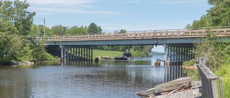 A wooden dock extending into a calm river with a bridge overhead.