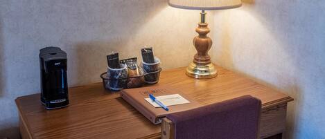 A wooden desk with a coffee maker, a lamp, a notebook, and a pen.