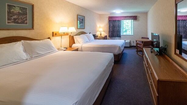 Habitación de hotel con dos camas, un escritorio con silla, televisor y ventana con cortinas.