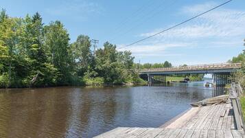 A wooden dock extending into a calm river, a bridge in the background, and lush greenery on the banks.