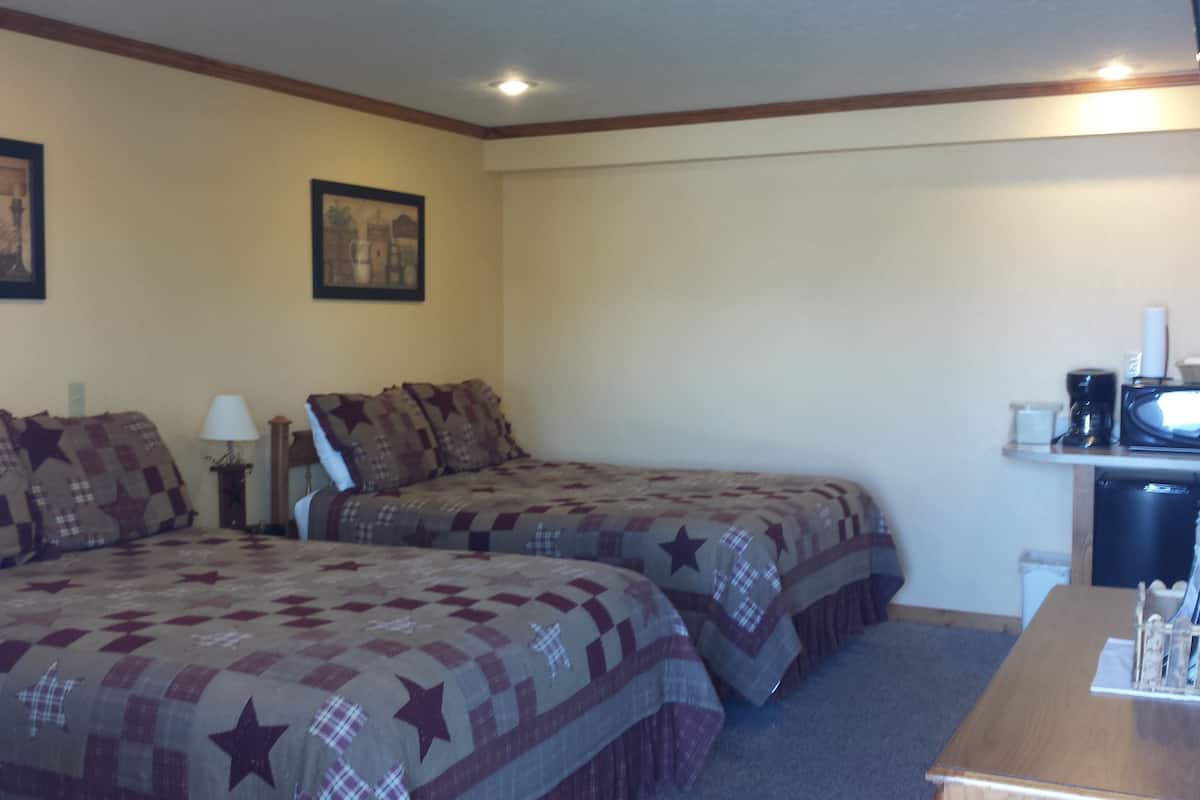 A hotel room with two beds, a desk, a lamp, and a microwave.