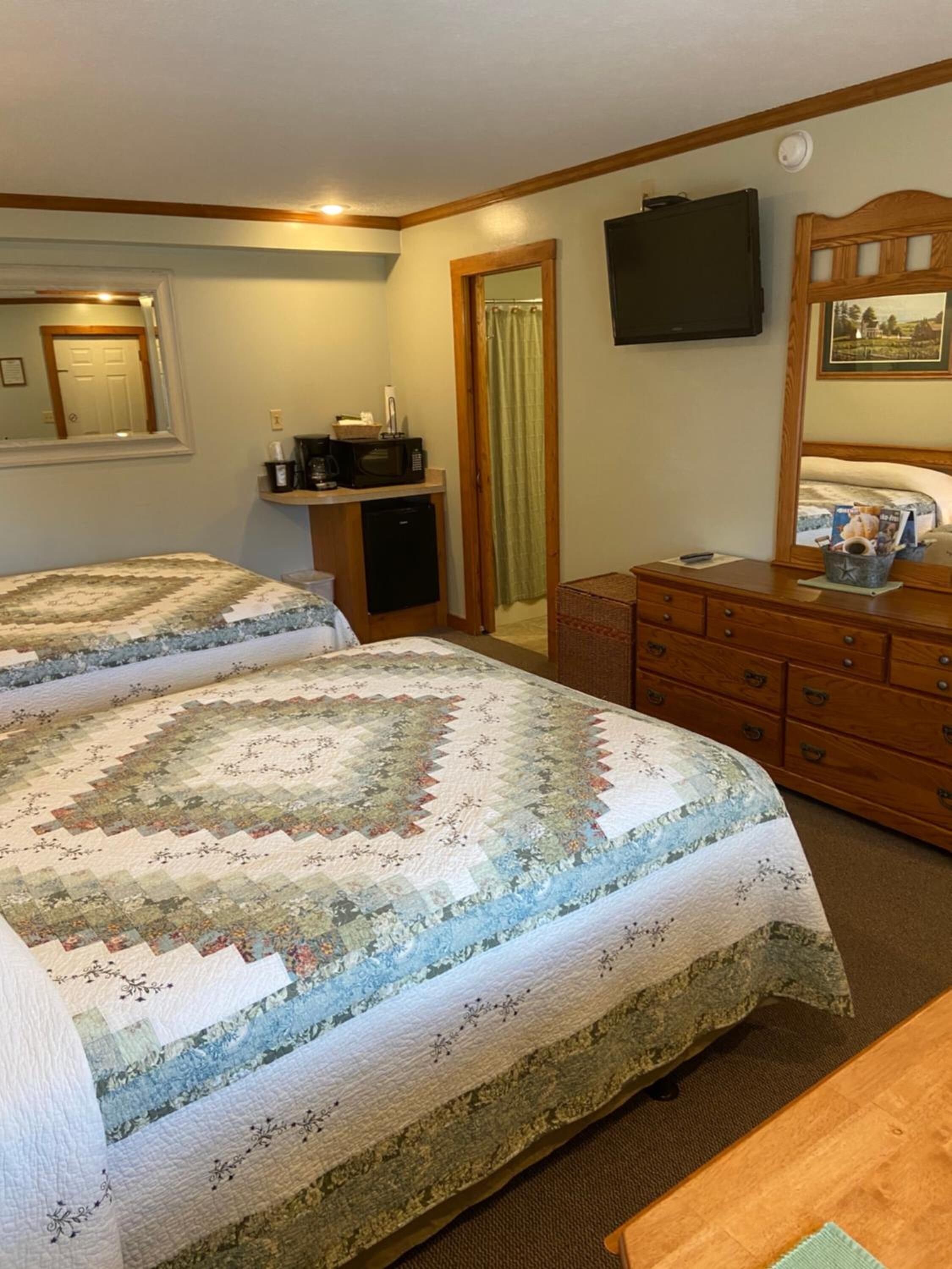 A bedroom with two beds, a dresser, a television, and a small kitchenette.