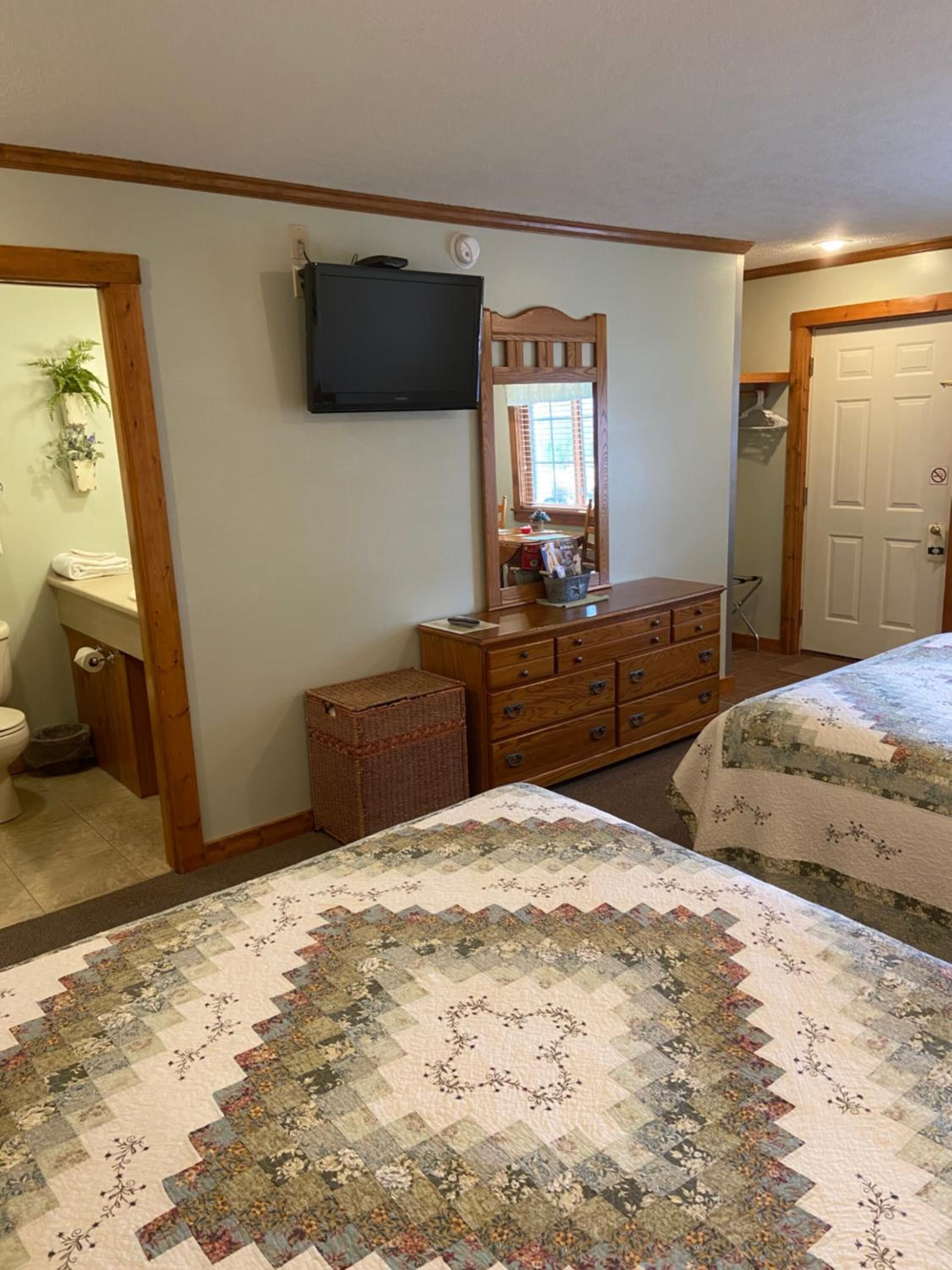 A bedroom with two beds, a dresser, a television, and a mirror.