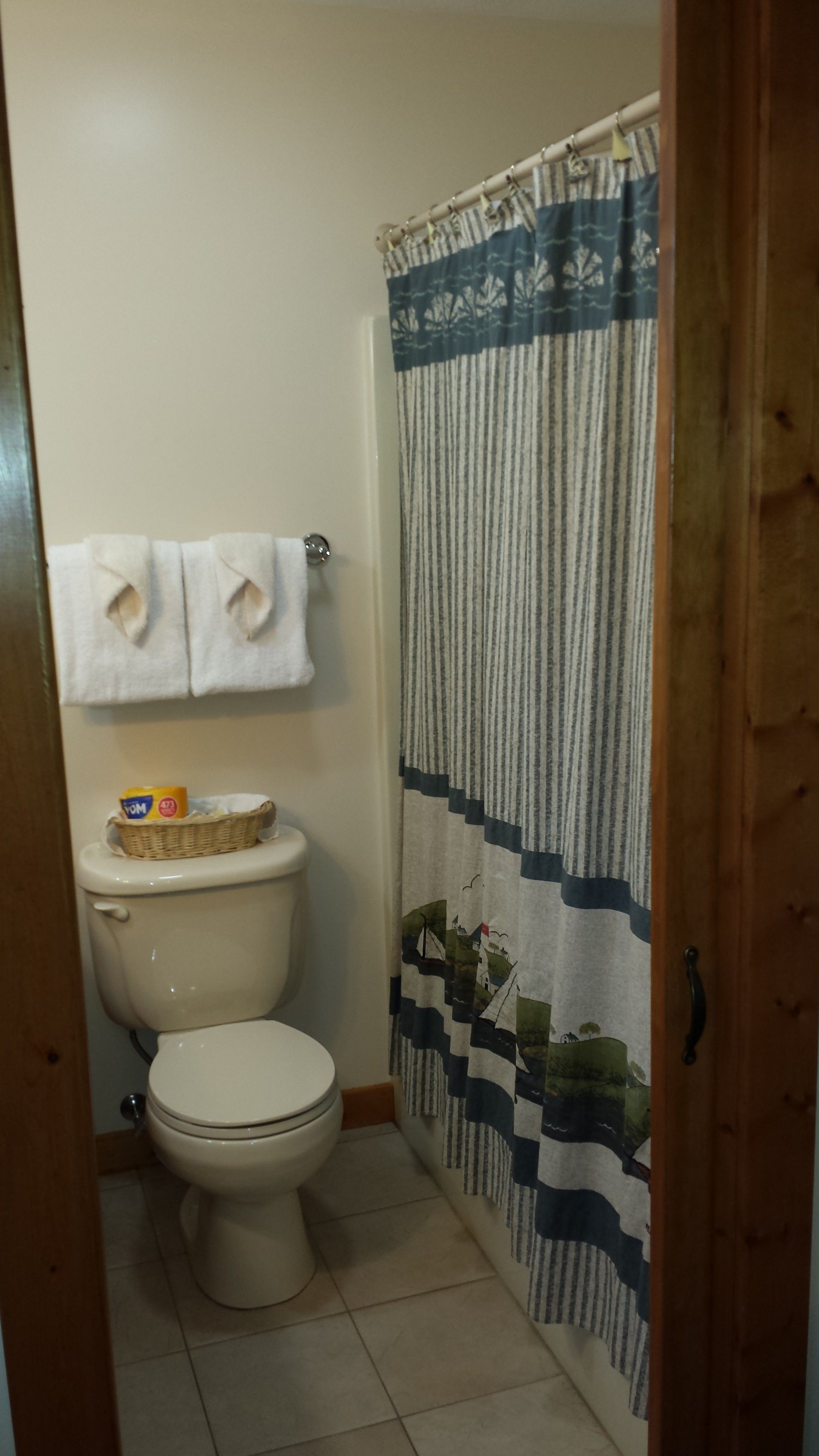 Une salle de bain équipée de toilettes, d’un panier contenant des articles de toilette et d’un rideau de douche à motifs nautiques.