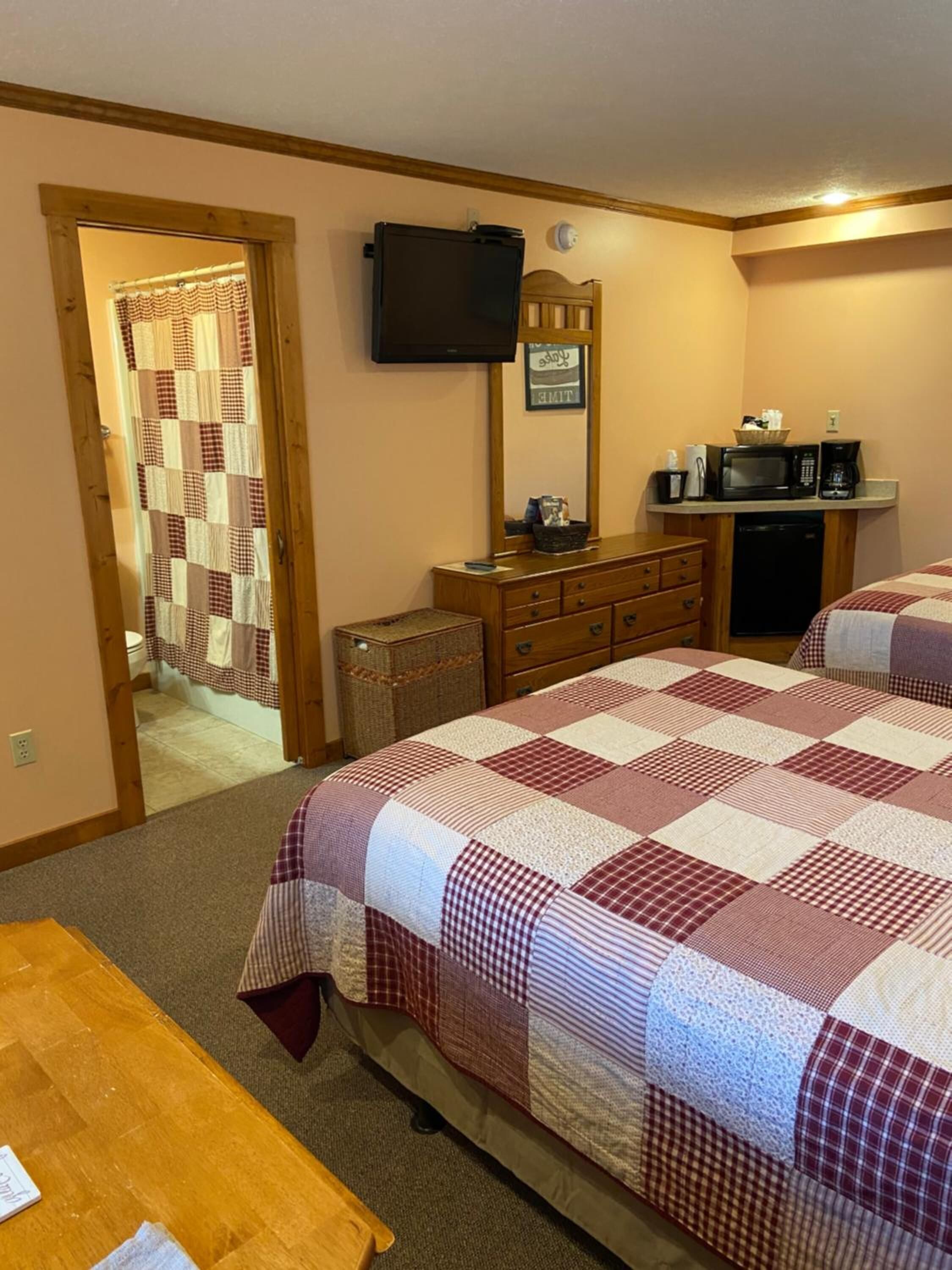 A hotel room with a bed, a wooden dresser, a microwave, a television, and a small kitchenette.