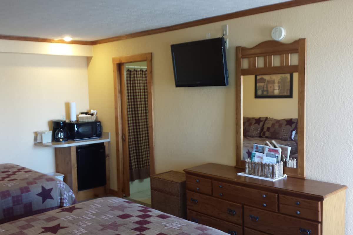 A hotel room with two beds, a dresser, a television, and a small kitchenette.