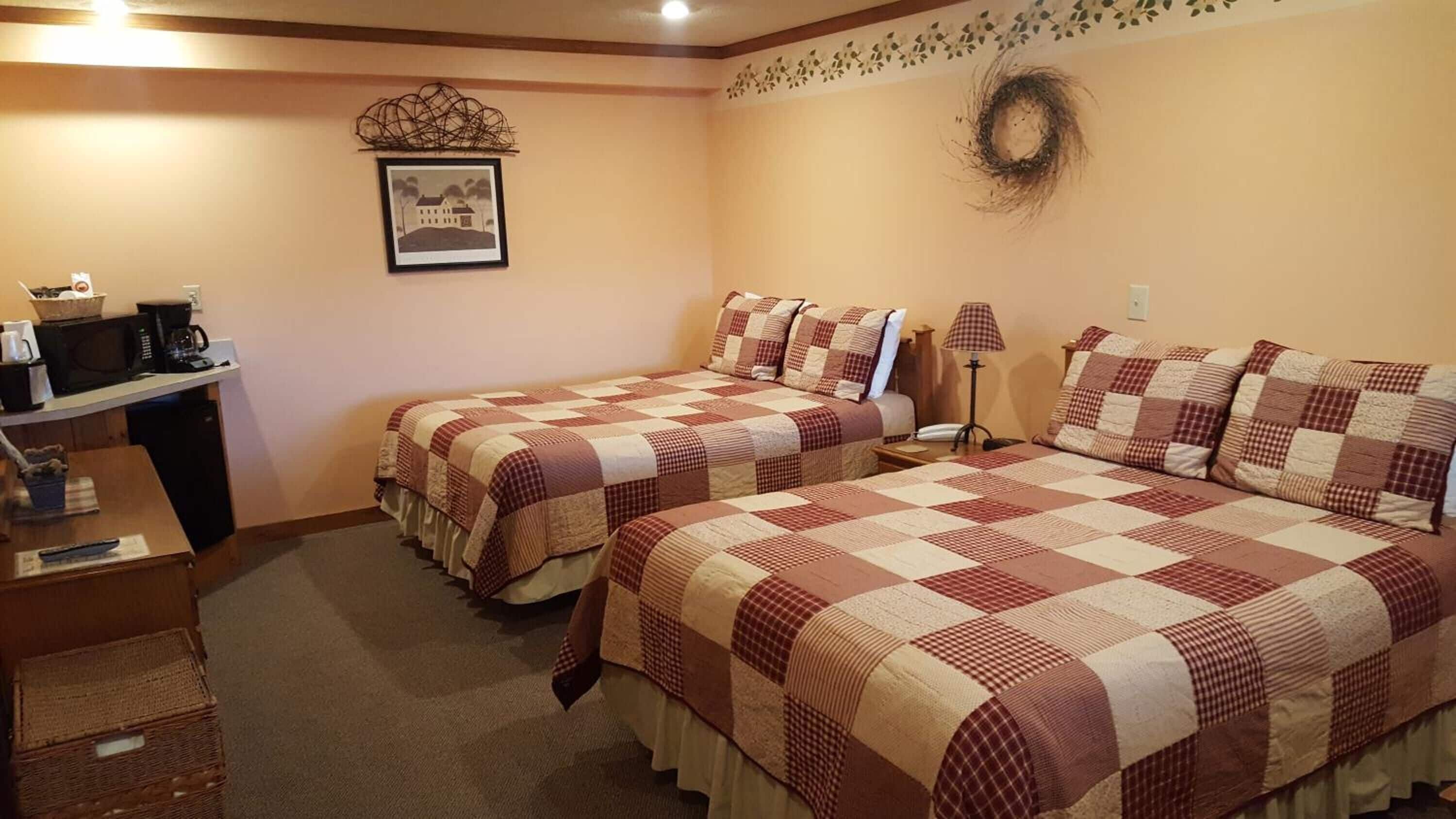 Habitación de hotel con dos camas, un escritorio con microondas, cafetera y un cuadro en la pared.