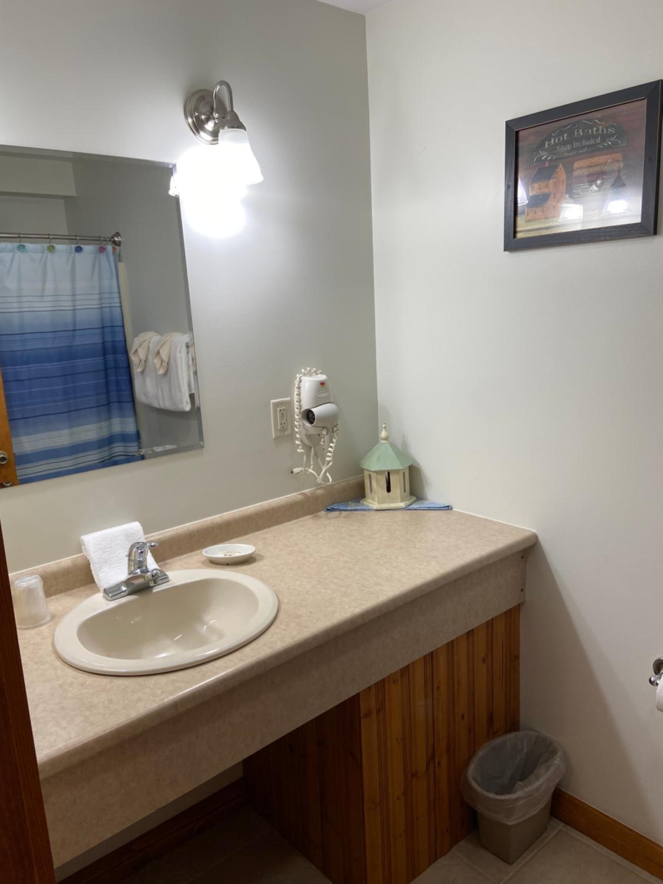 A bathroom with a sink, mirror, towel rack, and a framed sign above the mirror.