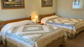 A room with two beds, each with a quilted bedspread, a nightstand with a lamp, and framed pictures on the walls.