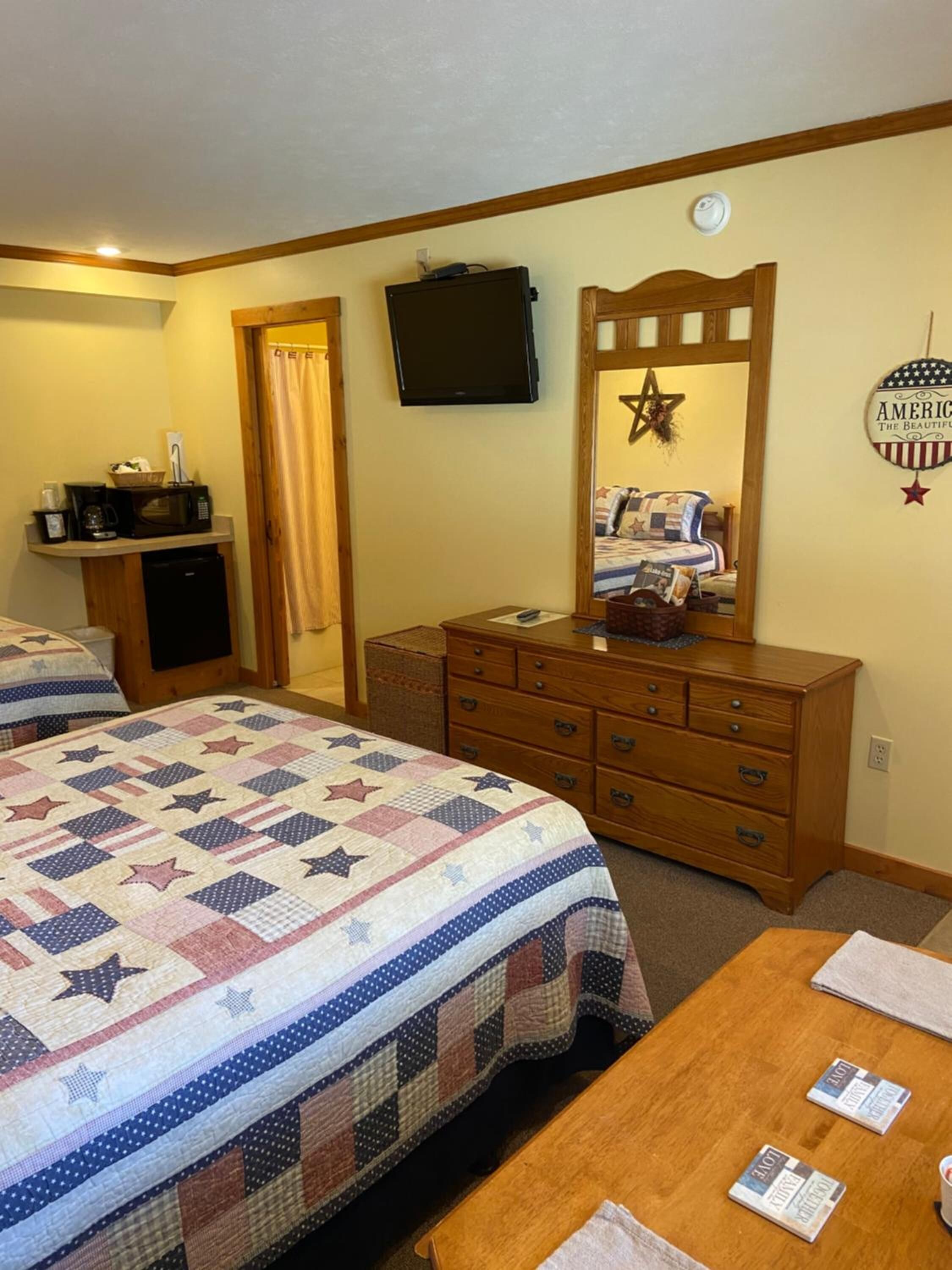 A hotel room with a large bed, a wooden dresser, a television, and a wall decoration.