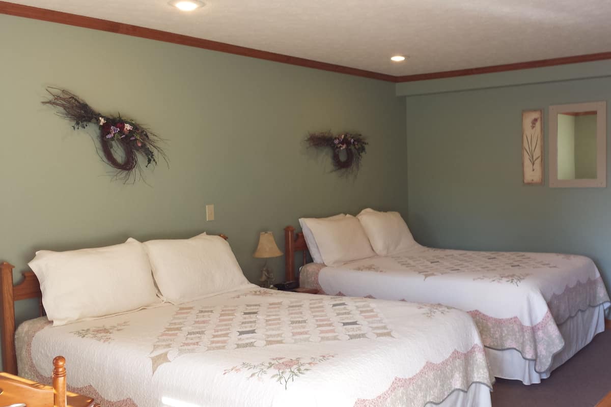A room with two beds, a wooden table, and a wall with two wall-mounted wreaths.