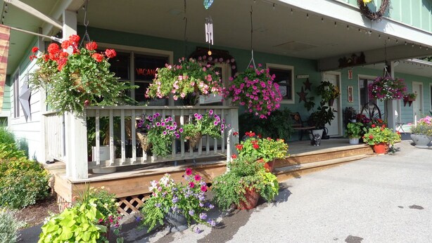 A porch with hanging flower baskets and potted plants. - The Garrett Inn (Oakland)