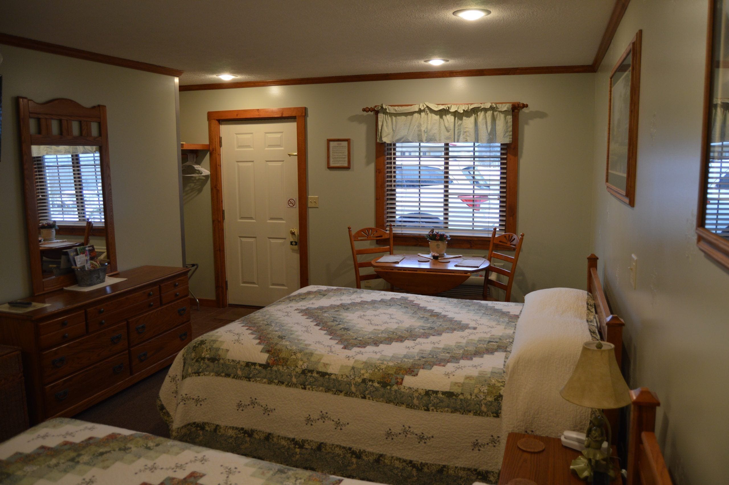 A bedroom with a bed, a desk, a chair, a dresser, and a window with blinds.