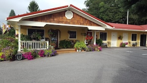 A motel with a red roof, a porch with potted plants, and a small outdoor seating area. - The Garrett Inn (Oakland)