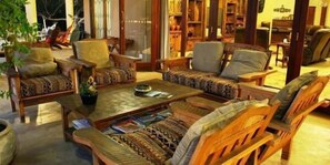 A cozy living room with wooden furniture, a coffee table with magazines, and a bookshelf filled with books. - Lion Tree Top Lodge (Hoedspruit)