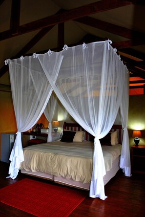 A four-poster bed with a canopy, a red rug, and wooden beams in the ceiling. - Lion Tree Top Lodge (Hoedspruit)