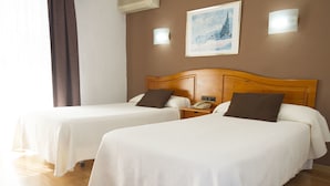A hotel room with two beds, a wooden headboard, a bedside table with a phone, and a painting on the wall.