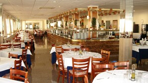 A spacious restaurant with multiple tables and chairs, a central bar area, and a long counter with a variety of dishes displayed.