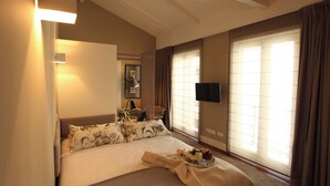 Habitación de hotel con cama, televisión de pantalla plana, ventana con cortinas y mesita de noche con lámpara.