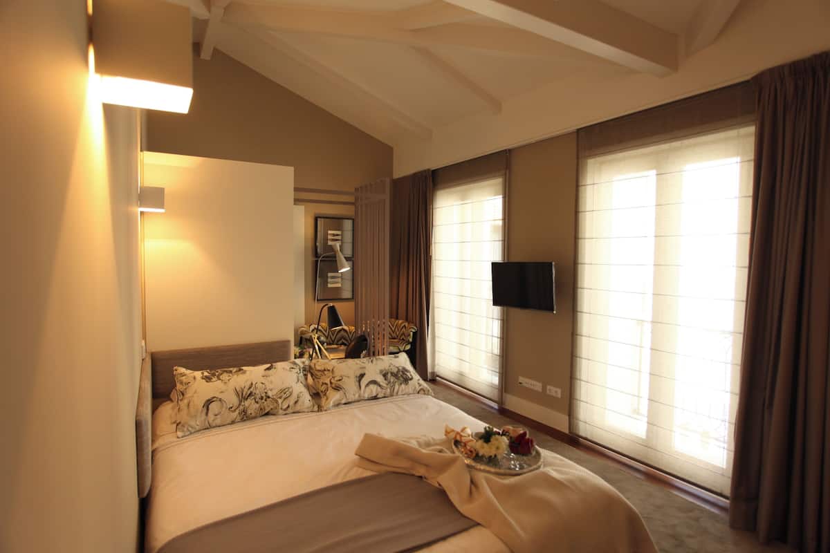 Habitación de hotel con cama, televisión de pantalla plana, ventana con cortinas y mesita de noche con lámpara.