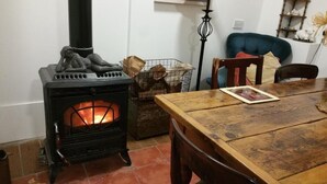 Um quarto acolhedor com uma lareira a lenha, uma mesa de jantar com cadeiras e uma poltrona azul estofada.