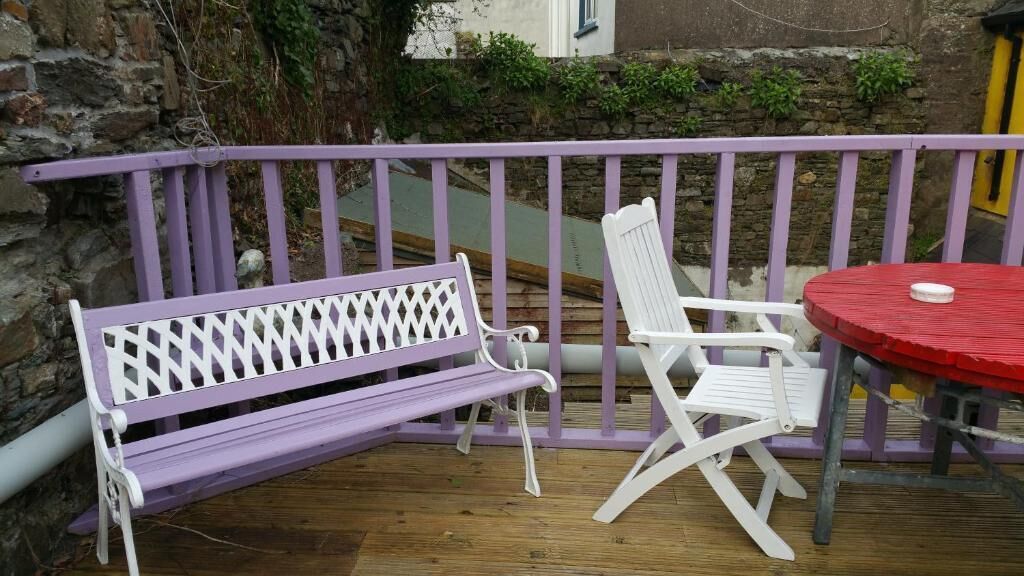 A wooden deck with a purple and white bench, a white folding chair, and a red table.