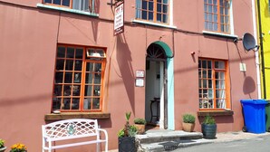 Um edifício rosa com várias janelas, um banco e vasos de plantas em frente.