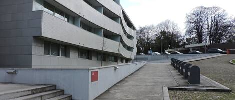 En modern byggnad med en fasad av betong, flera balkonger och en parkeringsplats med bilar.