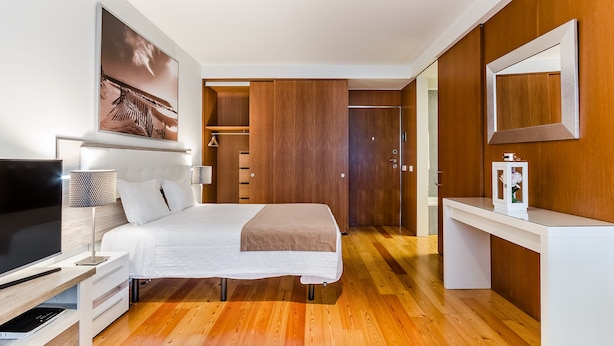 Une chambre d’hôtel moderne équipée d’un lit, d’une table de chevet, d’une télévision et d’un grand miroir.