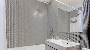 Une salle de bain moderne avec un mur de douche recouvert de carreaux noirs et blancs, une baignoire blanche et un meuble-lavabo avec un miroir.