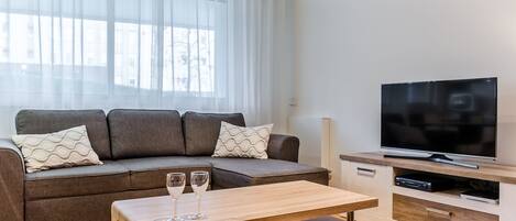Una sala de estar moderna con un sofá seccional gris, una mesa de centro de madera y un televisor de pantalla plana sobre un mueble de madera.