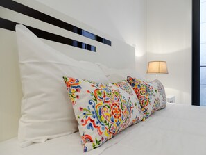 Uma cama com almofadas brancas e coloridas, um abajur e uma cabeceira moderna com linhas horizontais.