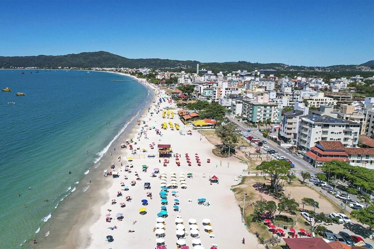 A coastal cityscape with a wide beach, numerous umbrellas, and buildings along the shore.