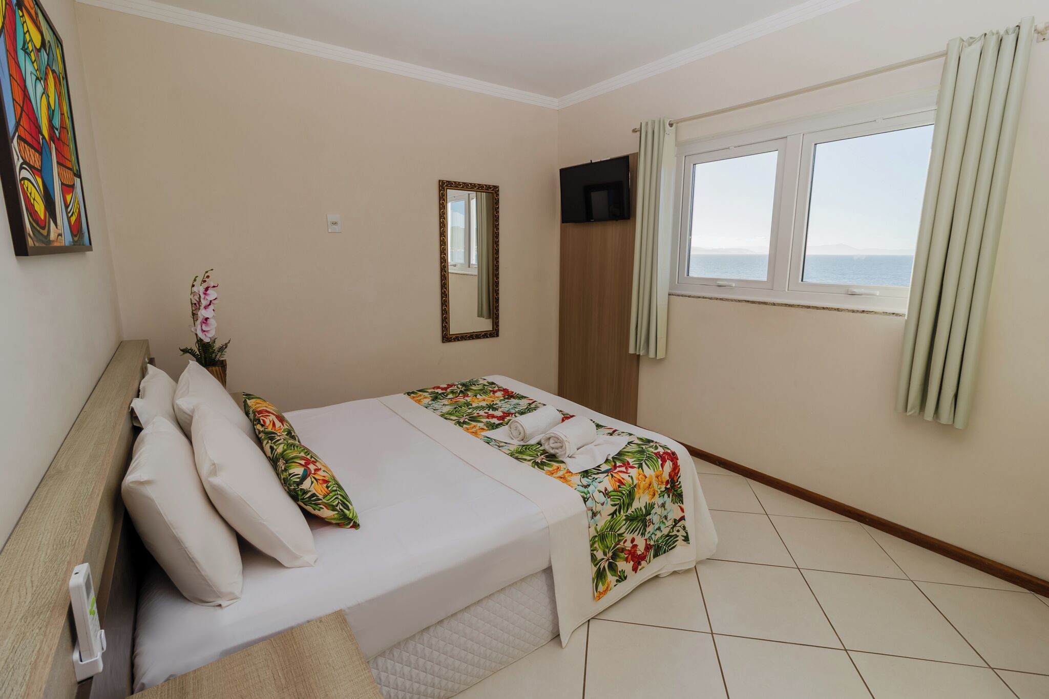 A hotel room with a bed, a TV, a window with curtains, and a painting on the wall.