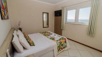 A hotel room with a bed, a TV, a window with curtains, and a painting on the wall.