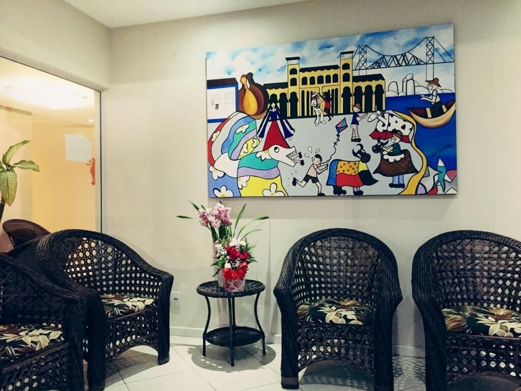 Un área de recepción con sillas de mimbre, una mesita con un jarrón de flores y un mural colorido que representa un paisaje urbano.