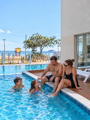 Una piscina con vista despejada al océano, una torre de salvavidas y una zona de playa con sombrillas.
