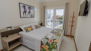 A hotel room with a bed, a bedside table, a TV, and a balcony with a view of buildings.