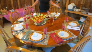 A wooden dining table set for a meal with a pineapple centerpiece, plates, cutlery, and a pitcher of drink. - Cupola Inn Bed & Breakfast (Nora Springs)