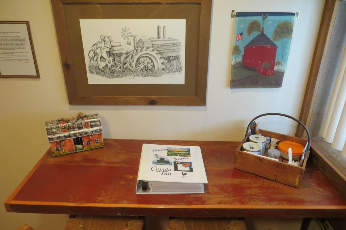 A wooden table with a framed drawing, a welcome brochure, and a basket with items.