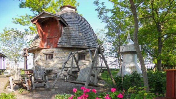 A rustic stone house with a conical roof, wooden furniture, and a small pond with pink flowers. - Cupola Inn Bed & Breakfast (Nora Springs)
